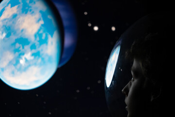 Child in a space suit observes a new planet to colonize. Concept: leaving the earth due to...