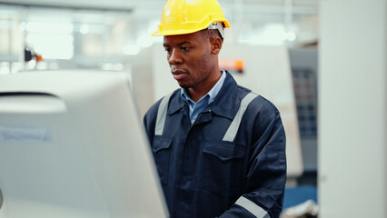 Portrait of African production engineer in safety wear operating CNC machine in the factory. A male factory worker concentrate on programming industrial machine to control the process of production.