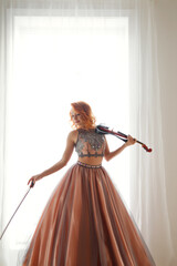 Chic cover woman posing with violin at large light window background, looking down away. Cute lady violinist in elegant art dress, holding playing violin. Music performance concept. Copy ad text space