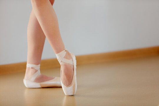 Cropped image of female legs standing on pointe in ballet studio school indoors. Classic ballet performer. Tender pastel colors. Concept of classical ballet, dance art, education, beauty, choreography