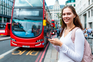 Smiling woman with smartphone at bus stop in London