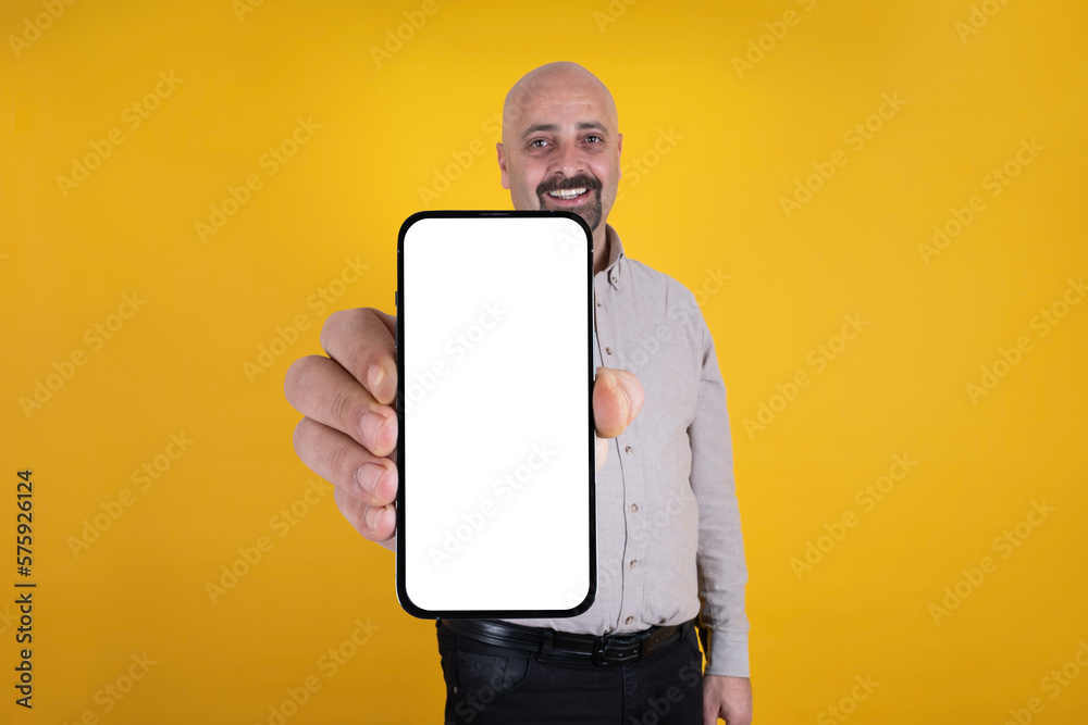 Wall mural smiling handsome caucasian bald guy showing empty blank screen of smartphone for mock up. standing w