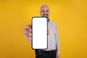 Fototapeta na wymiar Smiling handsome caucasian bald guy showing empty blank screen of smartphone for mock up. Standing warm orange studio background. Isolated and copy space. Mobile application recommend, advertisement.