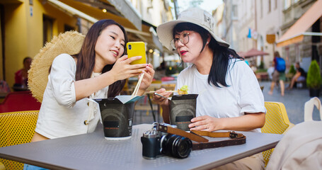 Portrait of joyful Asian mother and daughter sitting outdoor on restaurant terrace and eating chinese food. Young female having lunch with woman in cafeteria on street in city. Leisure concept