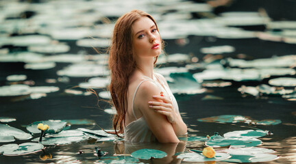 Beautiful red haired girl in white dress posing in river with water lilies. Fairytale story about ...