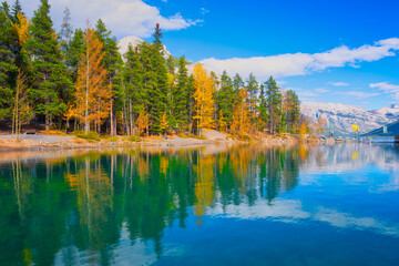 Mountain landscape at the day time. Lake and forest in a mountain valley. Natural landscape with a blue sky. Reflections on the surface of the lake.