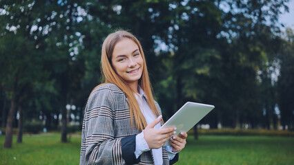 Fototapeta premium A young girl walks with a tablet in the park.