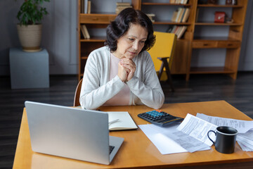 Middle aged senior woman sit with laptop and paper document. Pensive older mature lady reading...