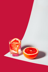 close-up on a summer cocktail with grapefruit next to half a grapefruit on a white-pink background
