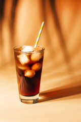close-up on a glass with cola and ice on a beige background with shadows