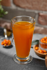 Orange tea on transparent cup. Homemade tea with sea-buckthorn isolation on concrete background. Vitamin tea with berries and citrus on upright glass on stone backdrop