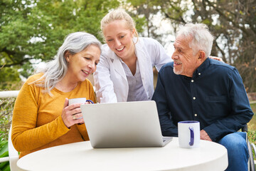 Doctor explaining elderly couple over laptop at table in garden