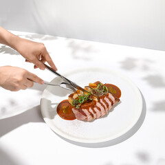 Young woman eat roasted duck breast with fork and knife. Female hand cuts duck fillet. Hands with knife and fork in trendy menu Eating food. Hands with food in summer menu concept