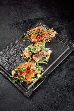 Assorted bruschetta in black concrete background. Antipasti set: tuna, salmon and roastbeef bruschetta on stone plate. Fish bruschetta and meat bruschetta in minimal style.