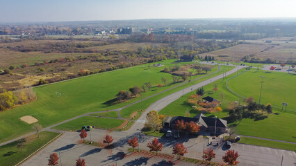 Aerial view community recreational center with grassy lawn soccer fields, colorful autumn leaves and plateau farm prairie leading to horizontal line in Rochester, New York