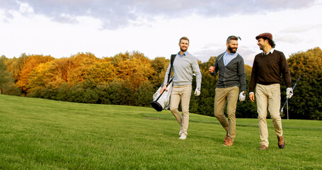 Attractive male friends walking with their clubs and bag on the golf pitch, talking and laughing.