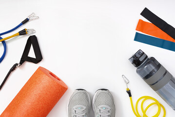 Fitness equipment on white background. Sports shoes, water bottle, orange Foam massage roll, fitness bands. Concept of healthy, wellness active lifestyle. Copy Space, Flat Lay