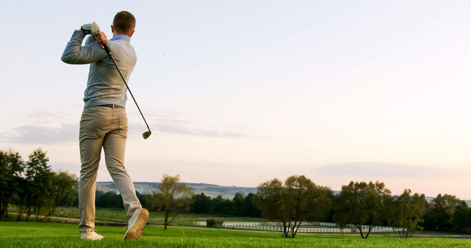 Handsome Caucasian golf player getting ready and hitting a ball with a club on a summer weather day. Outdoor. Golf field.