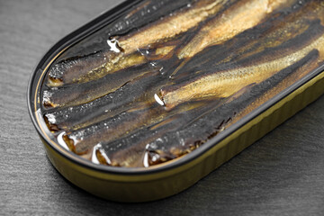 Sprats in oil, opened can of canned fish, on slate stone plate round, dark background selective focus