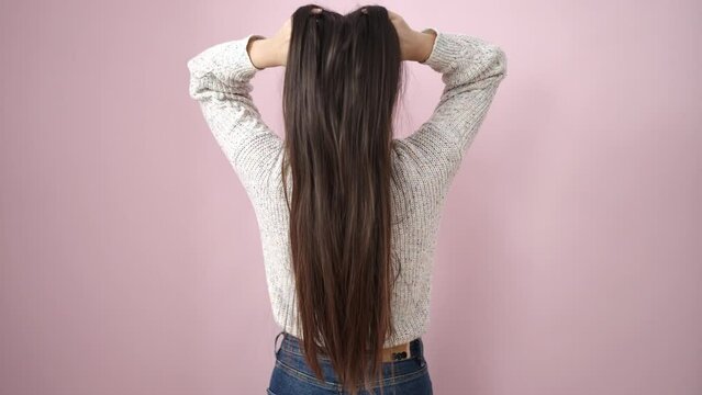 Young chinese woman combing hair with hands over isolated pink background