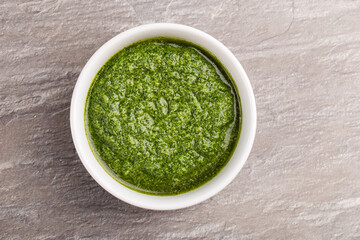 Top view on homemade pesto sauce with curly kale in a white bowl on a stone background. Healthy eating concept. Superfoods. Organic food.