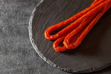 Pork or beef sausage, kabanos sausages, meat stick smoked close-up, on slate stone plate round, dark background