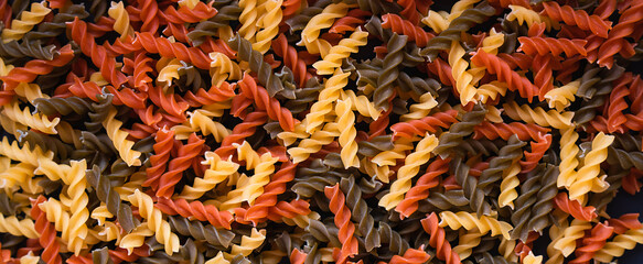 Tricolor fusilli paste spiral shape. Natural background. Banner. Close up. Top view. Selective focus.