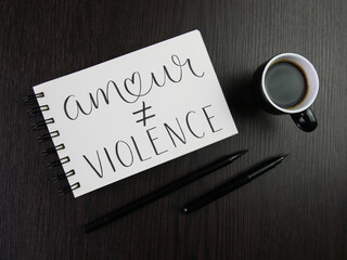 AMOUR ≠ VIOLENCE lettrage dans cahier avec tasse d'espresso et stylos sur bureau noir - obrazy, fototapety, plakaty