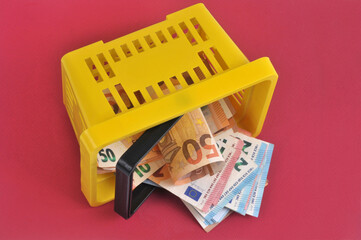 Panier en plastique jaune avec des billets de banque en euros renversé sur fond rouge