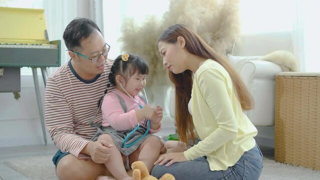 Asian Father and concentrated playful little preschool kid child daughter using stethoscope. Pretending to be a doctor nurse, listening smiling mommy breathing deeply, sitting floor at home.