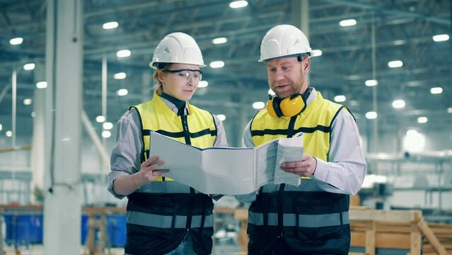 Two engineers are discussing factory documentation at modern factory facility.