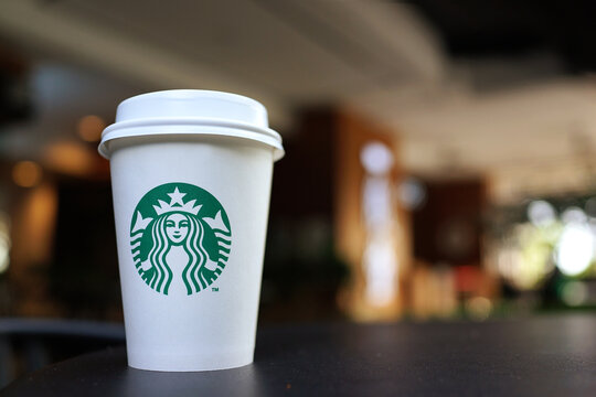PENANG, MALAYSIA - 22 FEB 2023: A white Starbucks coffee cup on table with bokeh interior background. Starbucks is the world's largest coffee house with over 20,000 stores in 61 countries.  