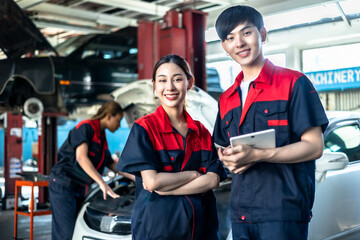 Asian  automotive engineer people wear helmet work in mechanics garage.young auto mechanic in uniform is looking at camera and smiling examining car.