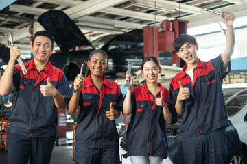 Engineer team checking under car condition on lifter in garage.Young auto mechanic in uniform is looking at camera and smiling examining car.