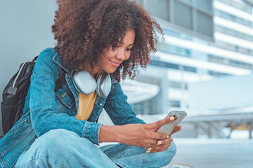 Smiling african american woman wearing headphones listening to music online from smartphone in the urban city. Female listening to music, song, podcast, or audiobook.
