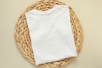 White folded t-shirt mockup on wicker table mat, front of blank shirt, space for design presentation.