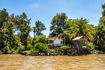 Boat tour on the Parana Delta, Tigre, Buenos Aires, Argentina. Palm trees, construction site of modern brick house. - obrazy, fototapety, plakaty
