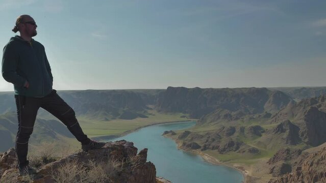 A guy stands on the edge of a cliff amid the magnificent landscape of a canyon with a turquoise river. Ili River in the spring. Kazakhstan. Alma-Ata's region
