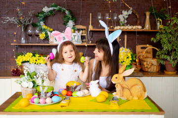 Easter, mom and daughter with Easter eggs and cake at the festive table are smiling and preparing for Easter at home in the kitchen in the ears of a hare.