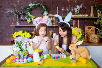 easter, mom and daughter paint Easter eggs with paint, smile and prepare for the holiday at home in the kitchen in the ears of a hare