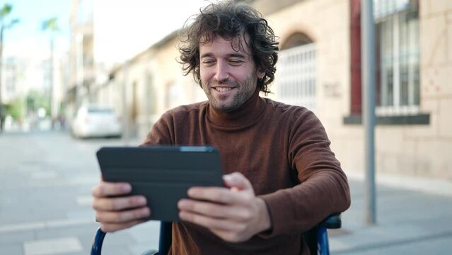 Young hispanic man using touchpad sitting on wheelchair at street