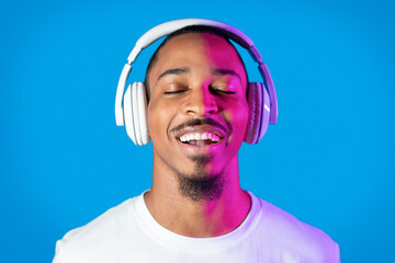 Joyful african american man listening to music, using wireless headphones