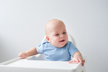 bald smiling baby boy 3 months sitting in baby chair on white background