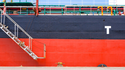Wide screen view of White gangway accommodation ladder of red and black of oil tanker while moored at harbor