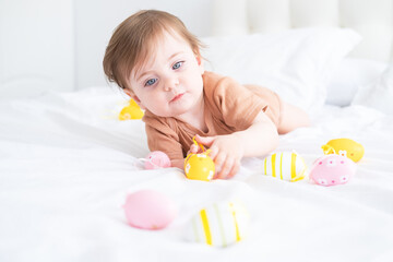cute funny baby with colorful Easter eggs on white bed at home