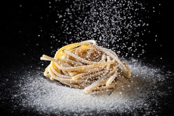 Uncooked traditional hand - rolled durum wheat pasta Pici of Tuscany, black background, macro photo of pasta pici and selective focus with white flour falling down