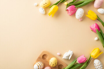 Fototapeta na wymiar Easter celebration concept. Top view photo of colorful easter eggs ceramic easter bunny tulips and wooden egg holder on isolated pastel beige background with empty space