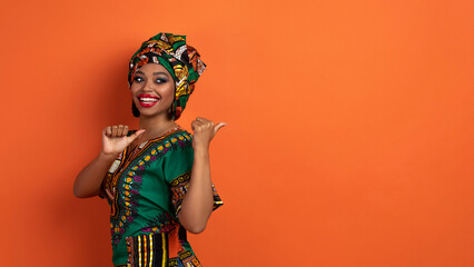 Stunning black woman in african costume pointing at copy space