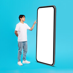 Japanese Teenager Guy Touching Huge Mobile Phone Screen, Blue Background