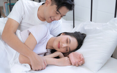 Fototapeta na wymiar Happy Asian couple lying down smiling and relaxing together in bed.